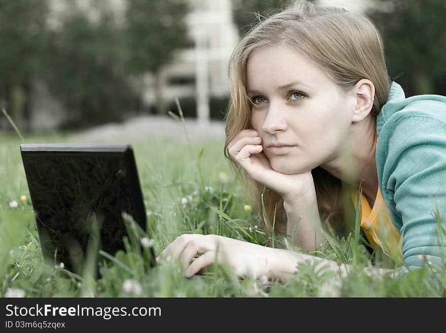 Portrait of pretty woman with laptop on the green grass