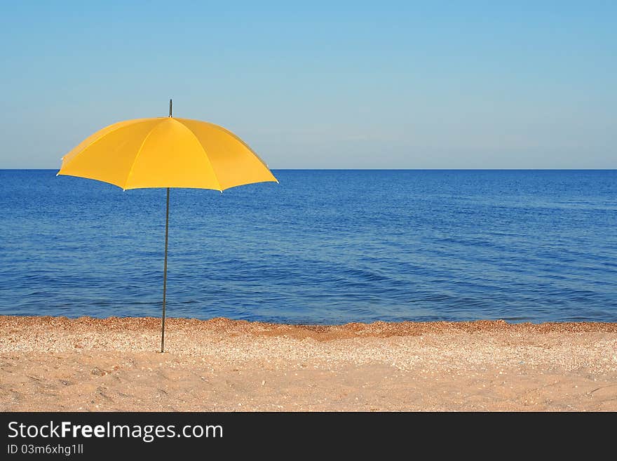 Yellow parasol, standing on the shore of the evening sea