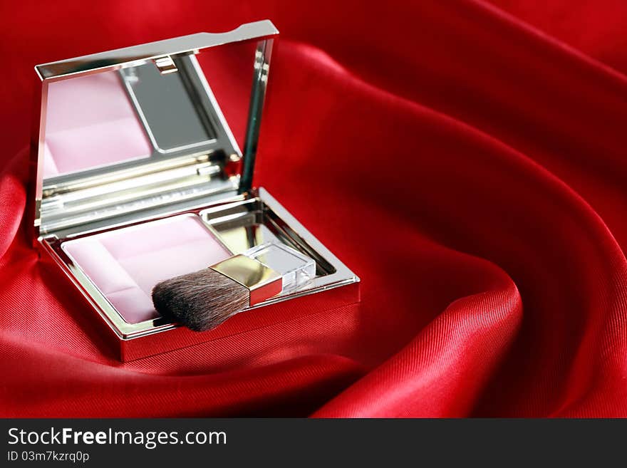 Open box with pink rouge and makeup brush on beautiful red silk. Open box with pink rouge and makeup brush on beautiful red silk