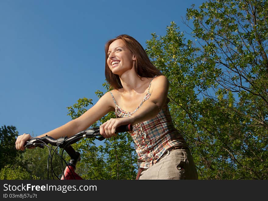 Pretty young woman with bicycle in a park smiling