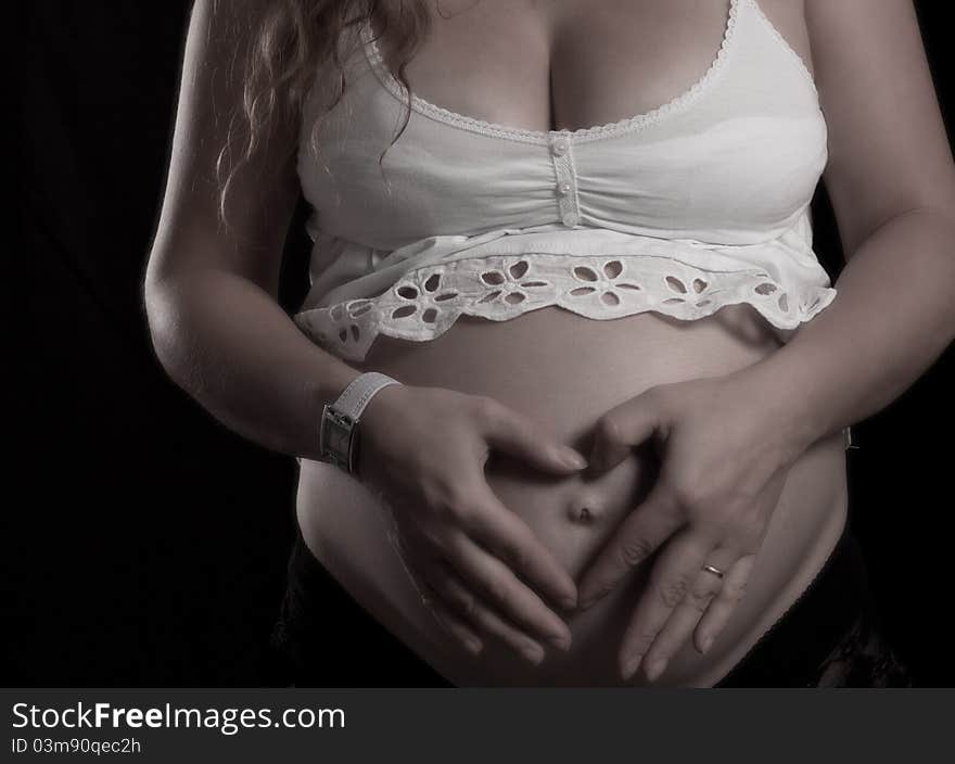 Heart shape hands on a pregnant women belly on black background. Heart shape hands on a pregnant women belly on black background