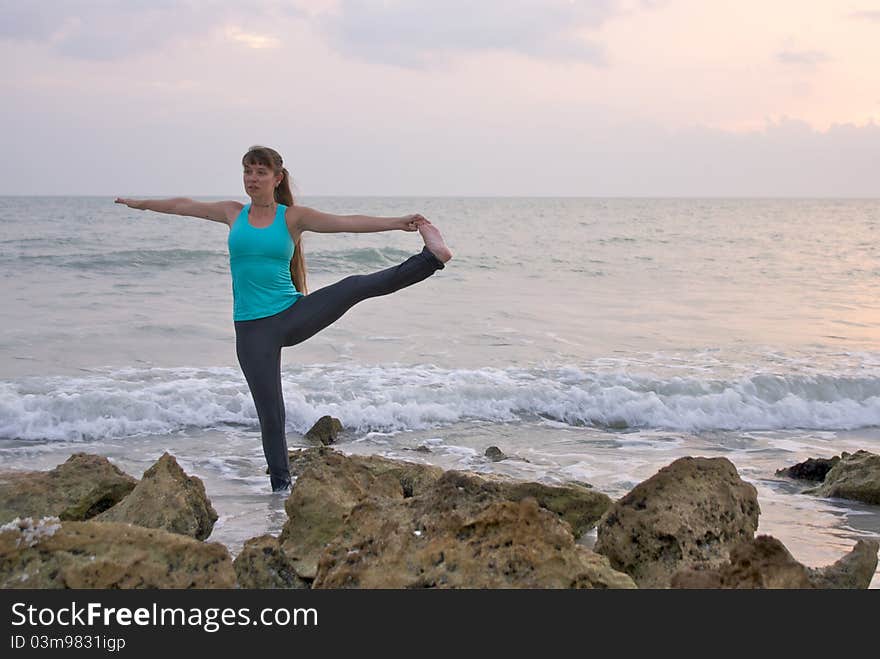 An athletic brown haired woman is doing yoga exercise extended standing hand to toe pose in the ocean water at the gulf of mexico in naples florida at sunset. An athletic brown haired woman is doing yoga exercise extended standing hand to toe pose in the ocean water at the gulf of mexico in naples florida at sunset.