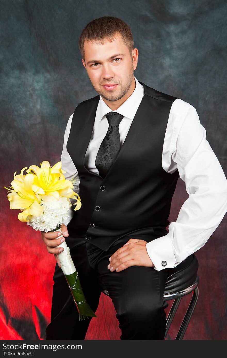 Young groom with a bouquet of yellow lilies in studio