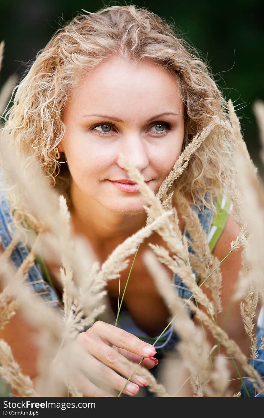 A beautiful blond haired blue eyed model wearing a sits amid tall grass