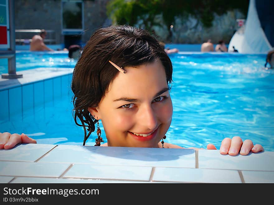 Close up portrait of a beautiful happy woman resting on her hands at the side of a sun bathed swimming pool