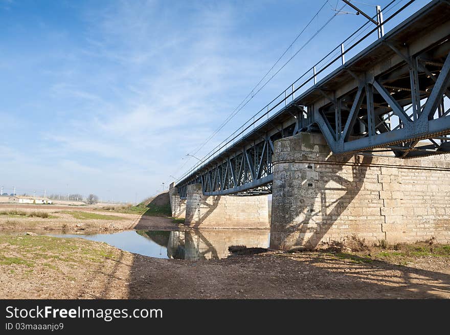 Old railway iron bridge over a narrow stream in an arable landscape in Ciudad Real Province, Spain. Old railway iron bridge over a narrow stream in an arable landscape in Ciudad Real Province, Spain