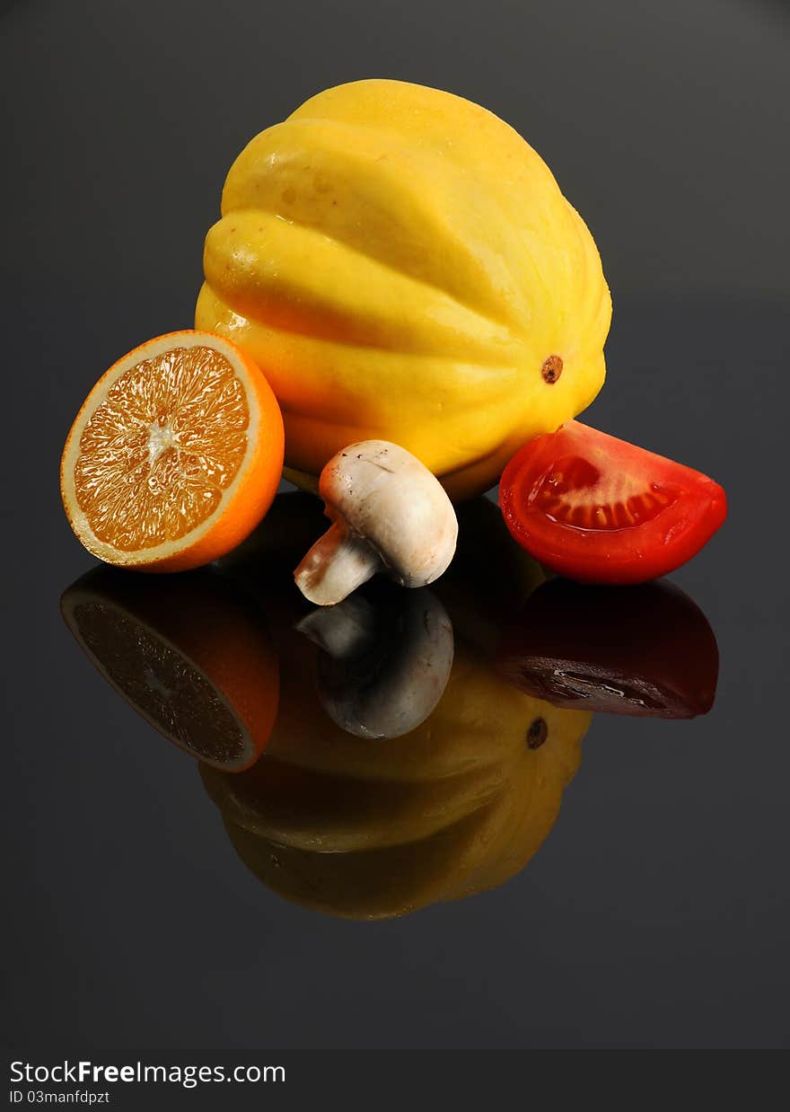 Slice of orange, squash; mushroom and tomato on reflective table. Slice of orange, squash; mushroom and tomato on reflective table