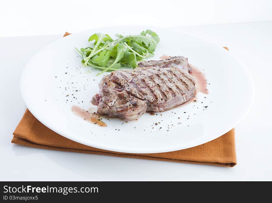 Grilled beef, served with arugula on a plate, view of the table with a white background