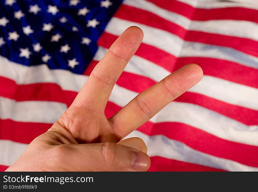 A hand holds up a peace sign in front of an American Flag. A hand holds up a peace sign in front of an American Flag.