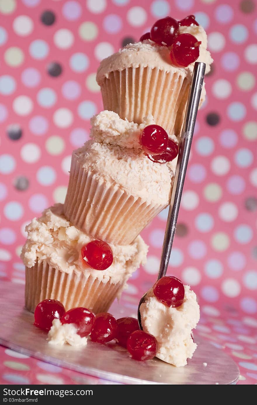 Stacked cupcakes with icing and glacé cherries and fun polka dot background. Stacked cupcakes with icing and glacé cherries and fun polka dot background