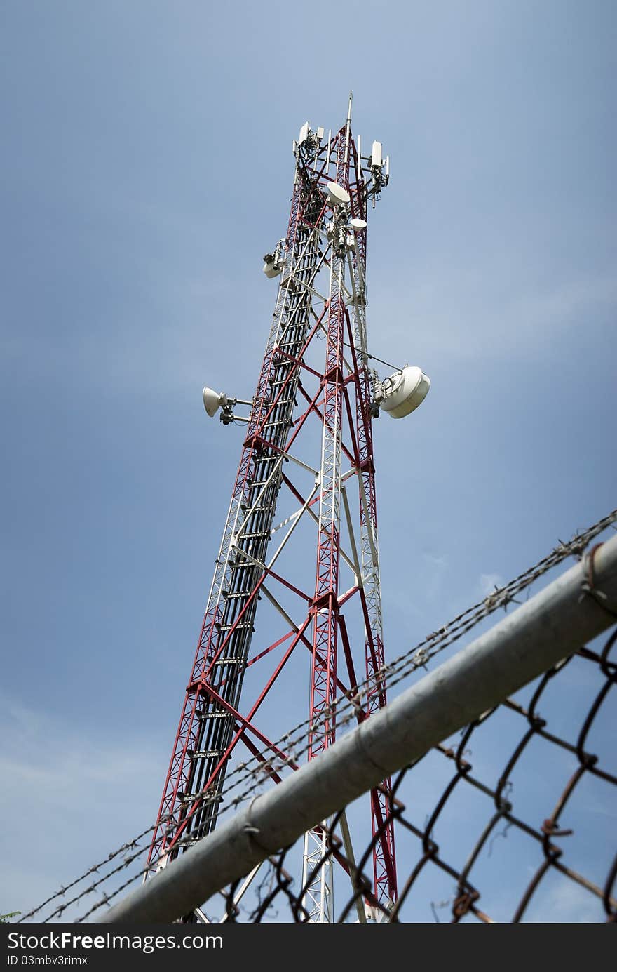 Radio communication tower against blue sky behind chain link fence and barbed wire. Radio communication tower against blue sky behind chain link fence and barbed wire