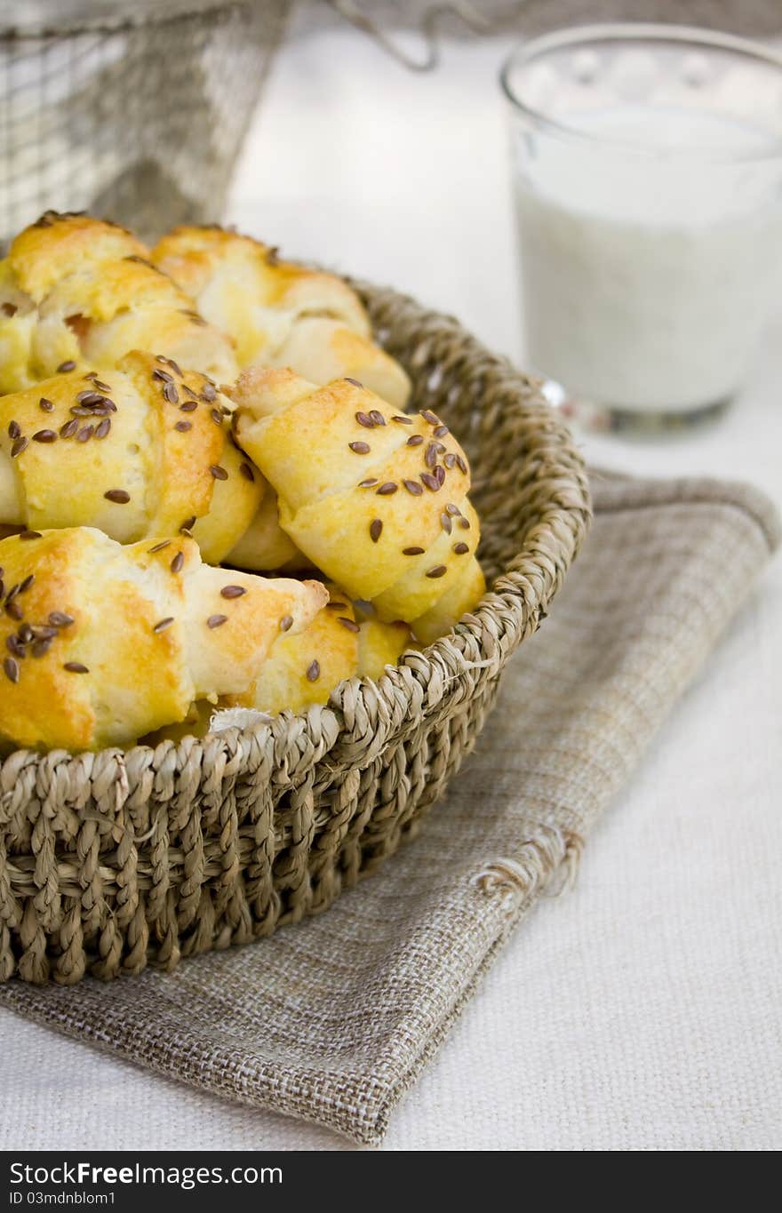 Home made baked buns in a basket, on the table, with a glass of milk