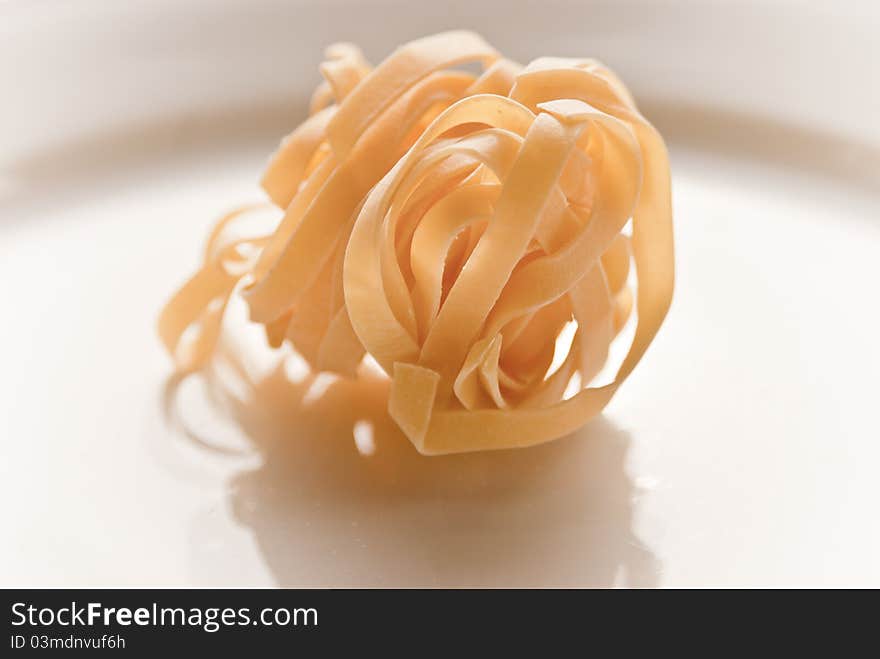 A plate of dried tagliatelle pasta shot in natural sunlight on a white plate