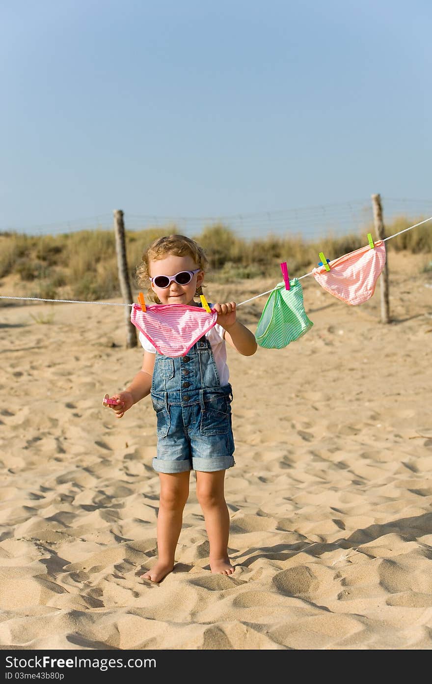 Little baby is hanging laundry on the beach