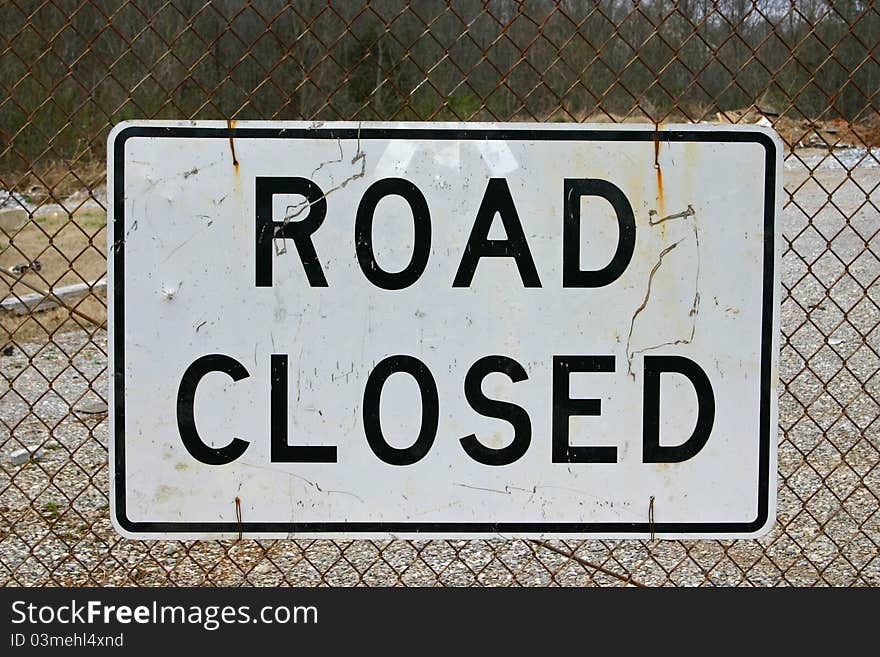 A road closed sign fastened to a chain link fence