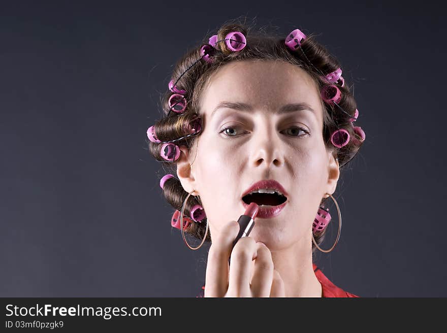 Beautiful girl in a red robe home paints her lips on a gray background closeup