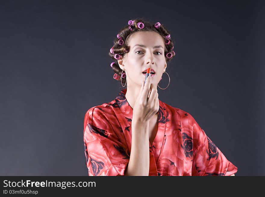 Beautiful girl in a red robe home paints her lips on a gray background closeup