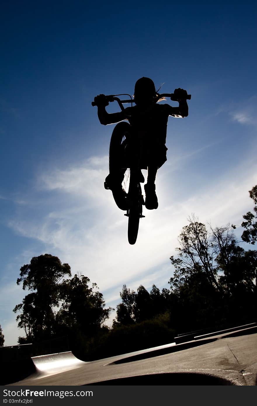 Silhouette of Freestyle BMX rider getting air at a skate park