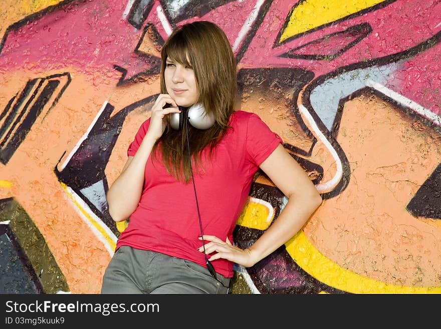 Beautiful brunette girl with headphones and graffiti wall at background.