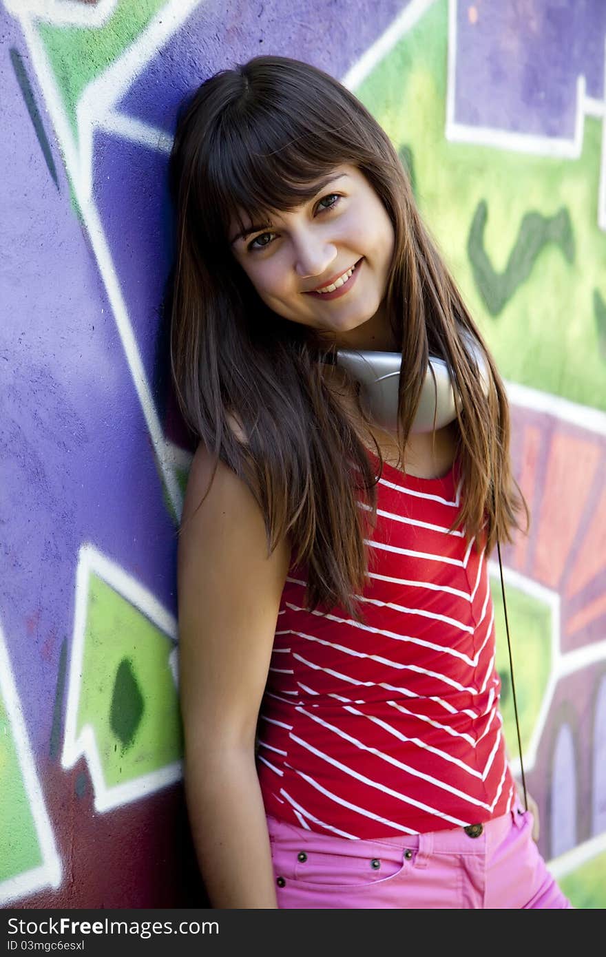 Beautiful brunette girl with headphones and graffiti wall at background.