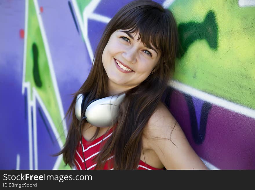 Beautiful brunette girl with headphones and graffiti wall at background.