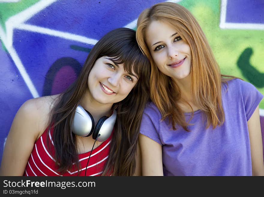 Two girlfriends near graffiti wall.