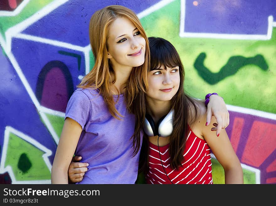 Two girlfriends near graffiti wall.