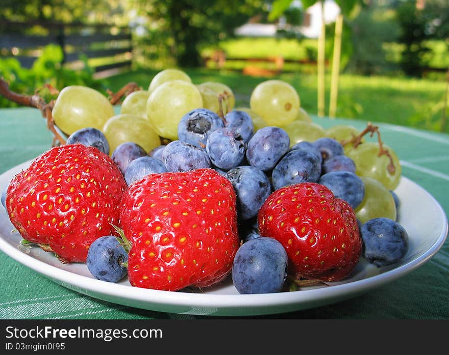 Delicious and Healthy Fruit Plate including strawberries, blueberries and grapes, served on the garden terrace on a sunny summer day. Hmmm... Just bite!