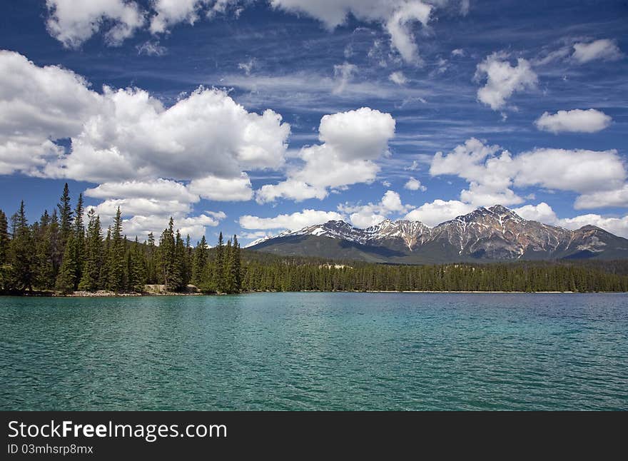 Lake Beauvert in Jasper National Park on a beautiful sunny day. Turquoise water and bright blue sky with puffy white clouds. Pyramid Mountain is in the distance.