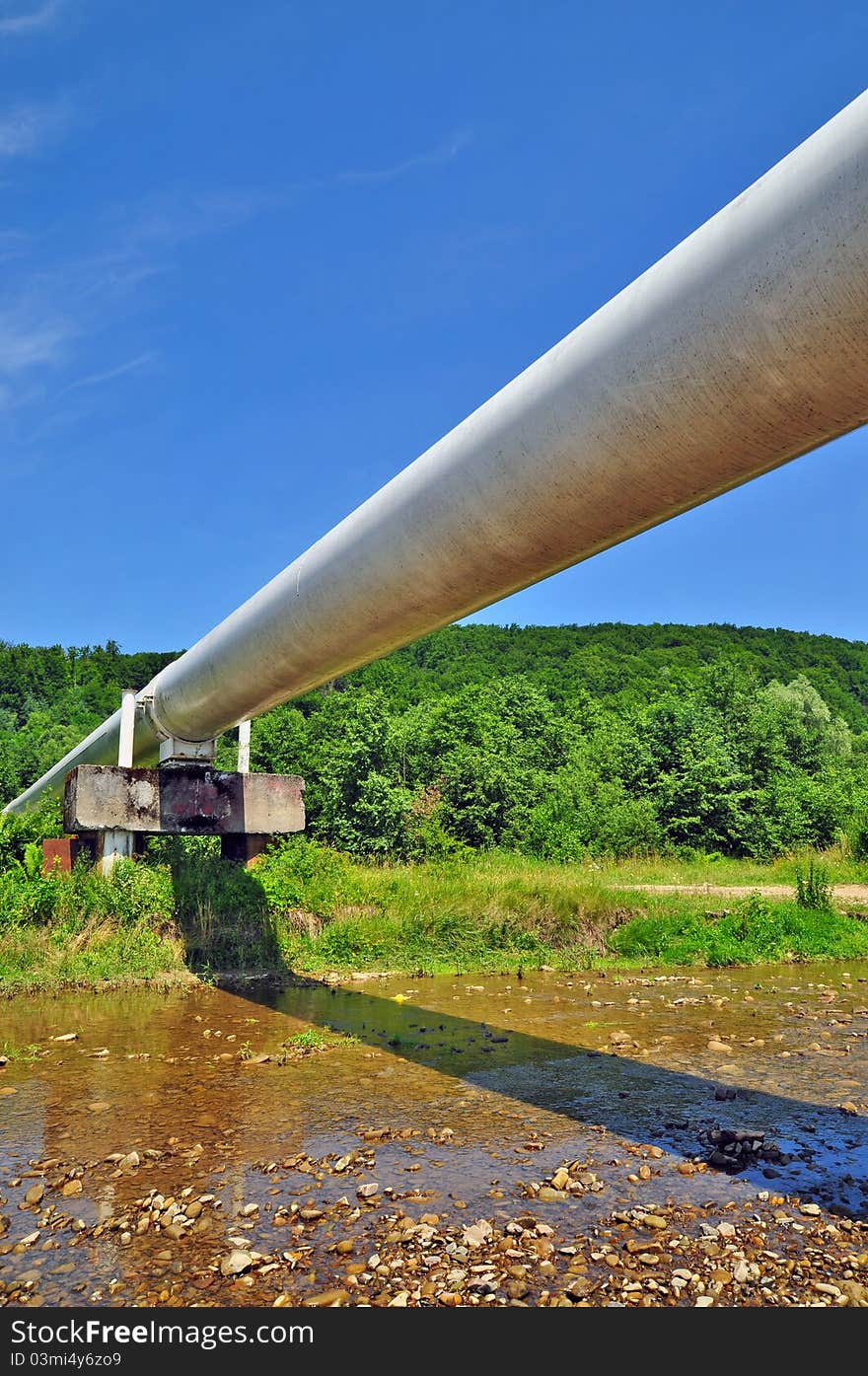 The high pressure pipeline in a summer landscape with the dark blue sky and clouds.