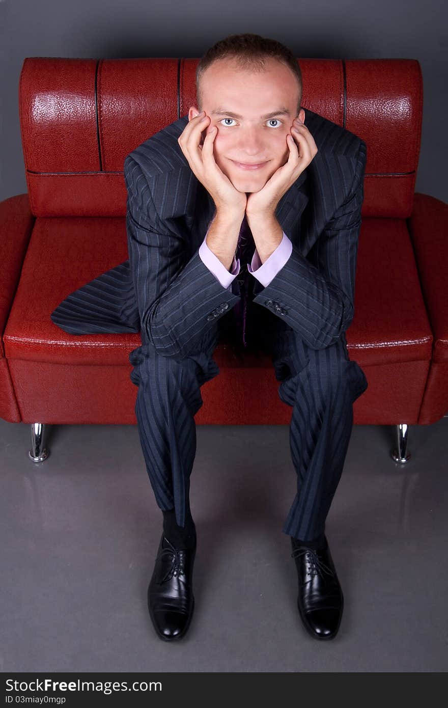 Thoughtful young man in a suit sitting on a red couch. Thoughtful young man in a suit sitting on a red couch