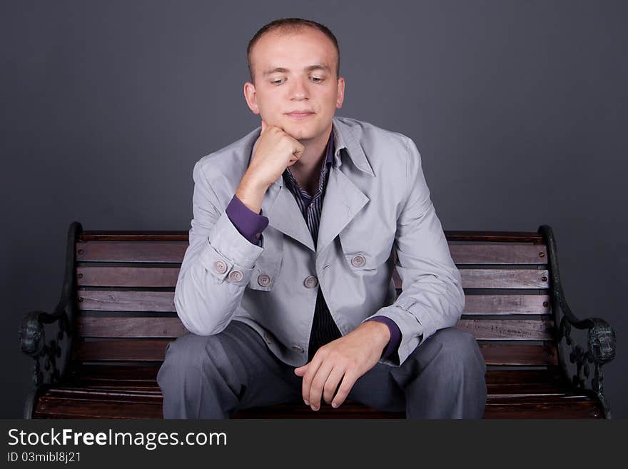 A man in a gray cloak sits on a street bench brown