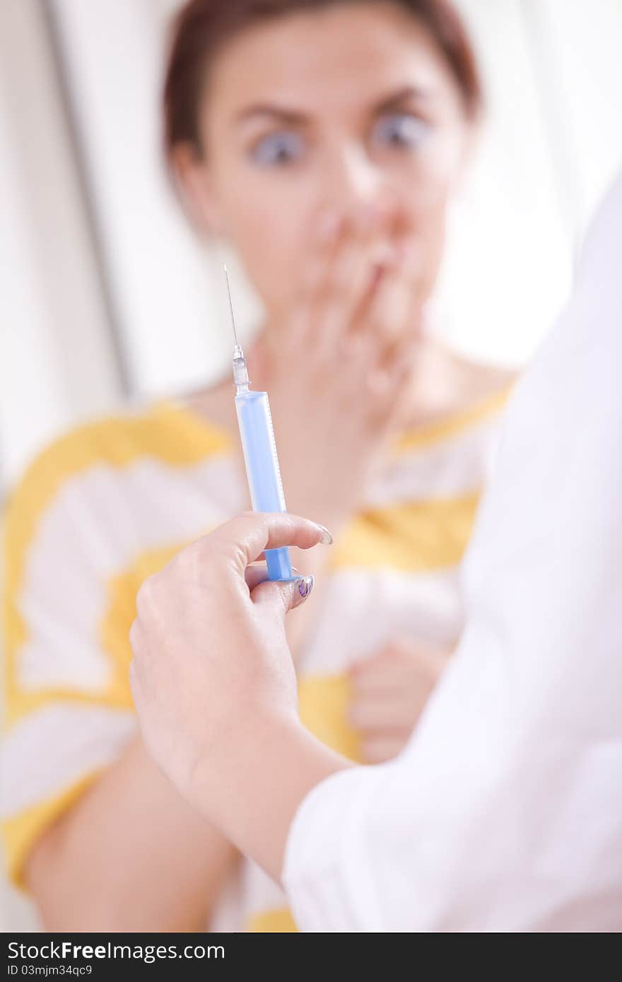 Doctor preparing vaccination injection - patient in fear on background. Focus on syringe and hand. Doctor preparing vaccination injection - patient in fear on background. Focus on syringe and hand.