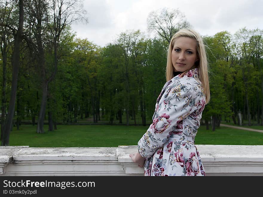 Blonde Girl Standing Against A Background Of Park