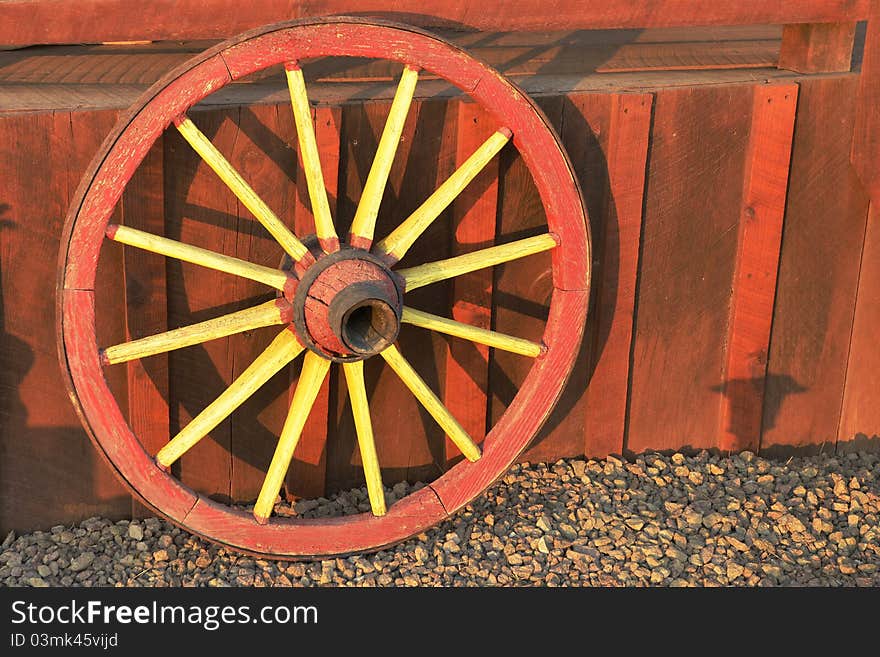 A colorful red and yellow antique wagon wheel leaning against a redwood porch