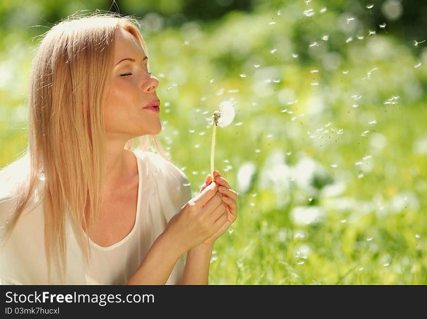 Girl blowing on a dandelion lying on the grass