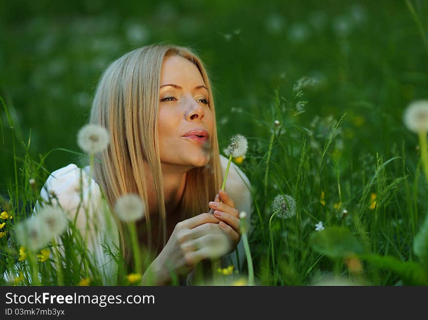 Girl blowing on a dandelion lying on the grass