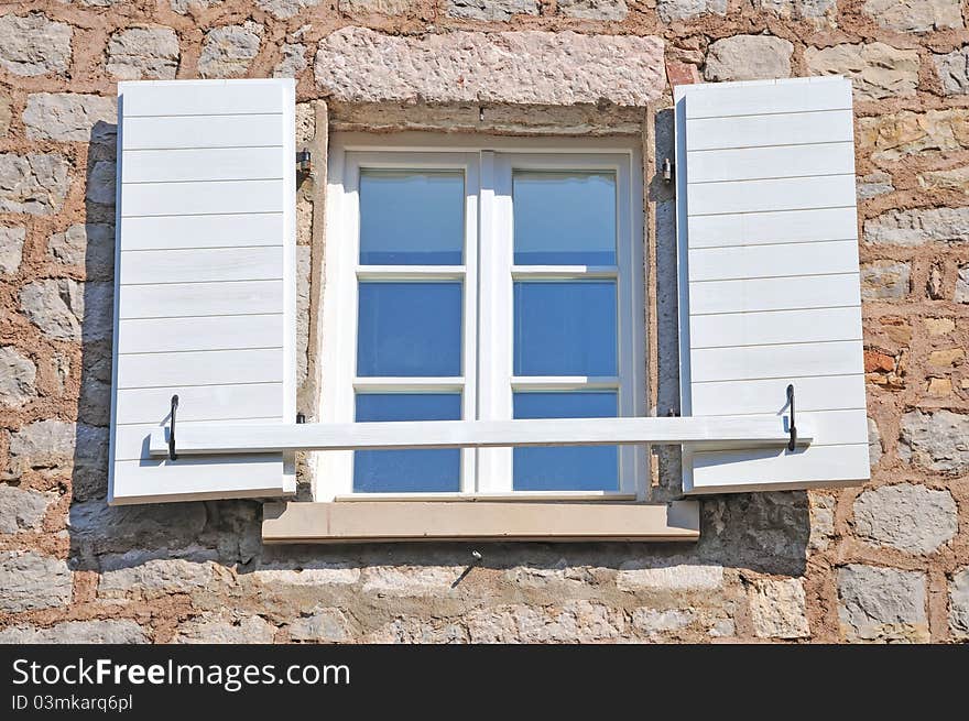 Open Mediterranean window, with stone wall and reflection of the blue sky