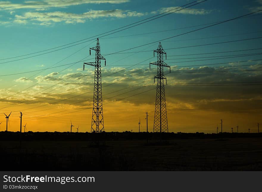 Silhouettes of electricity pillars and wind turbines on sunset