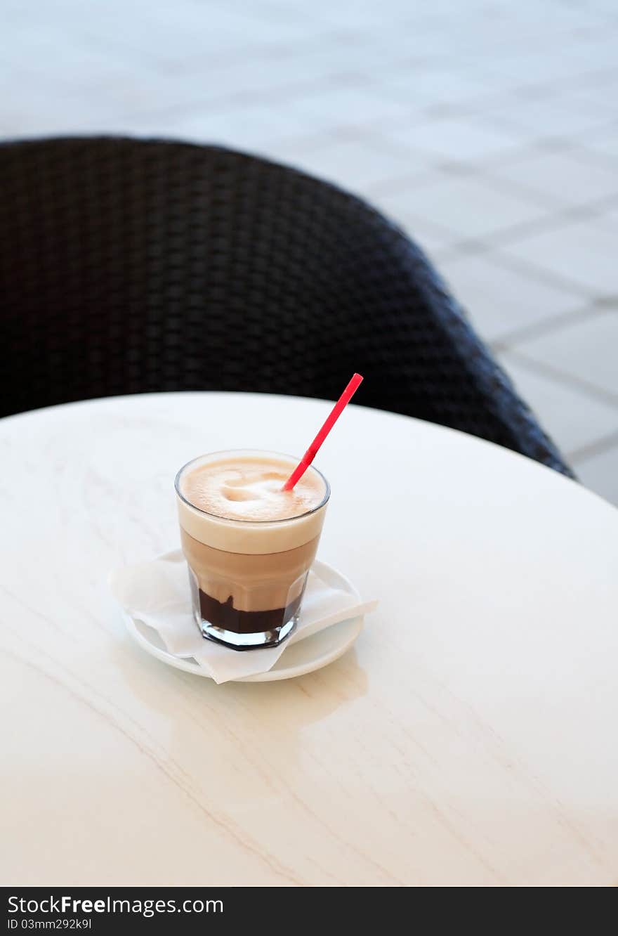 Glass of cappuccino standing on ring table near chair. Glass of cappuccino standing on ring table near chair