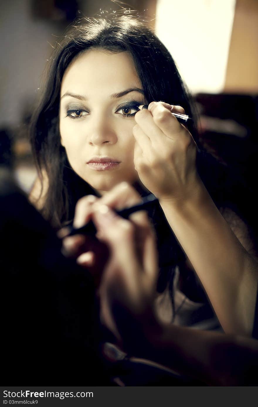 Beautiful young woman looking in mirror paint eyes