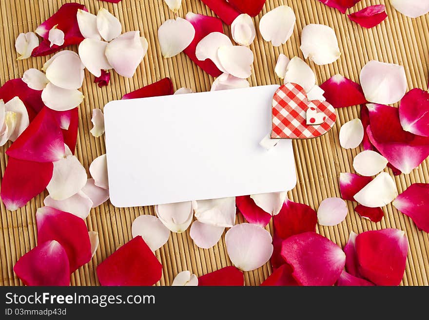 At the rose petals is white piece of paper and a red heart. Postcard. At the rose petals is white piece of paper and a red heart. Postcard