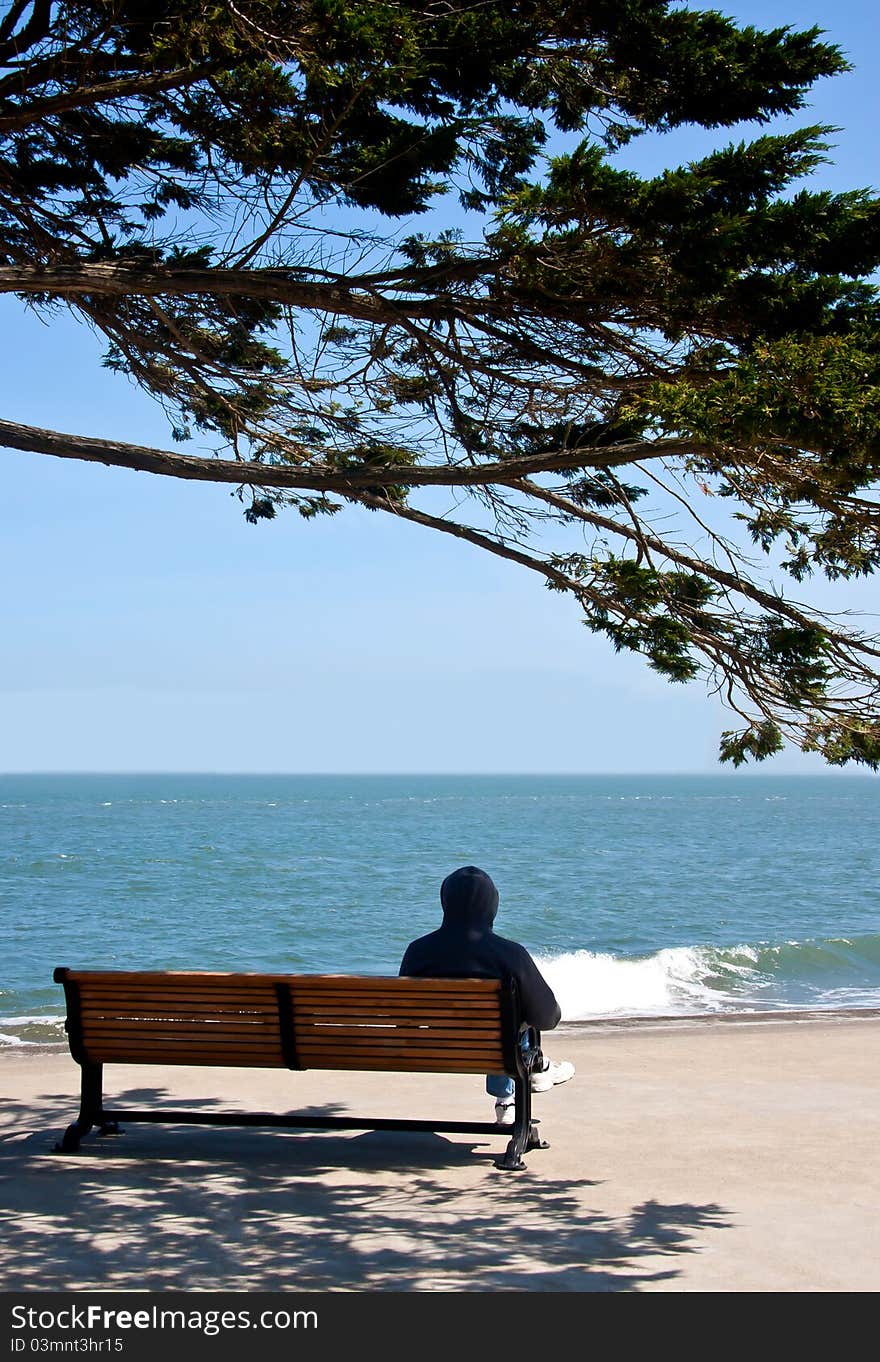 A man is sitting on a bench and looking to the sea. A man is sitting on a bench and looking to the sea