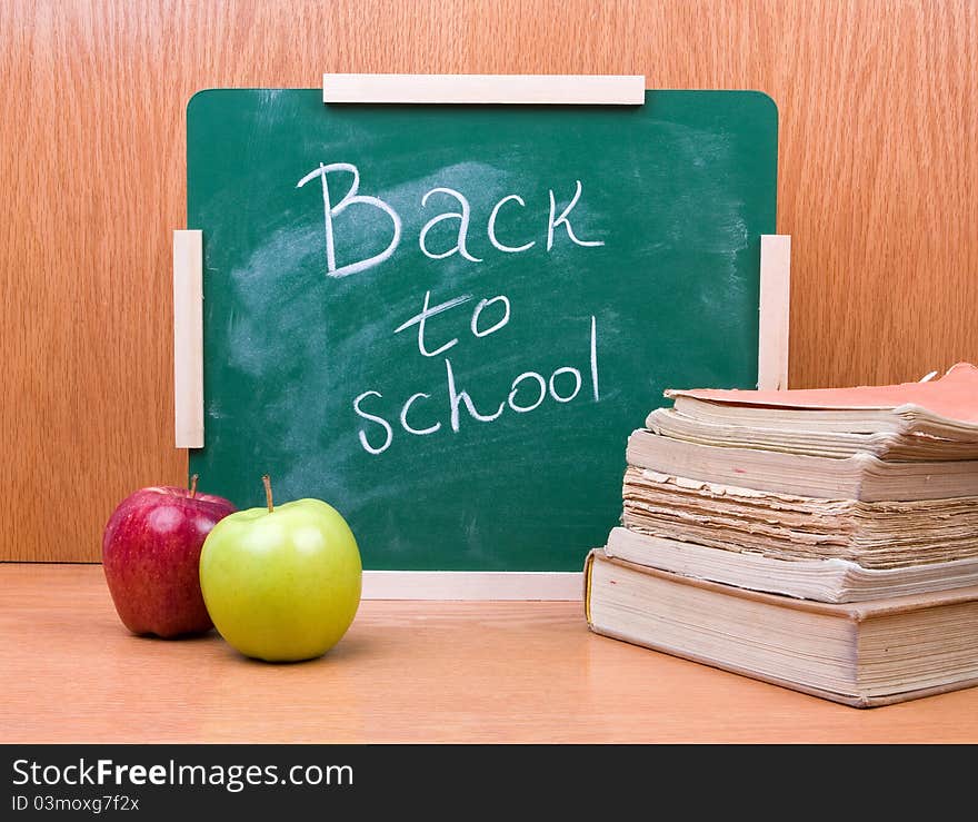 Back to school written on board with books and apples on the wooden table. Back to school written on board with books and apples on the wooden table