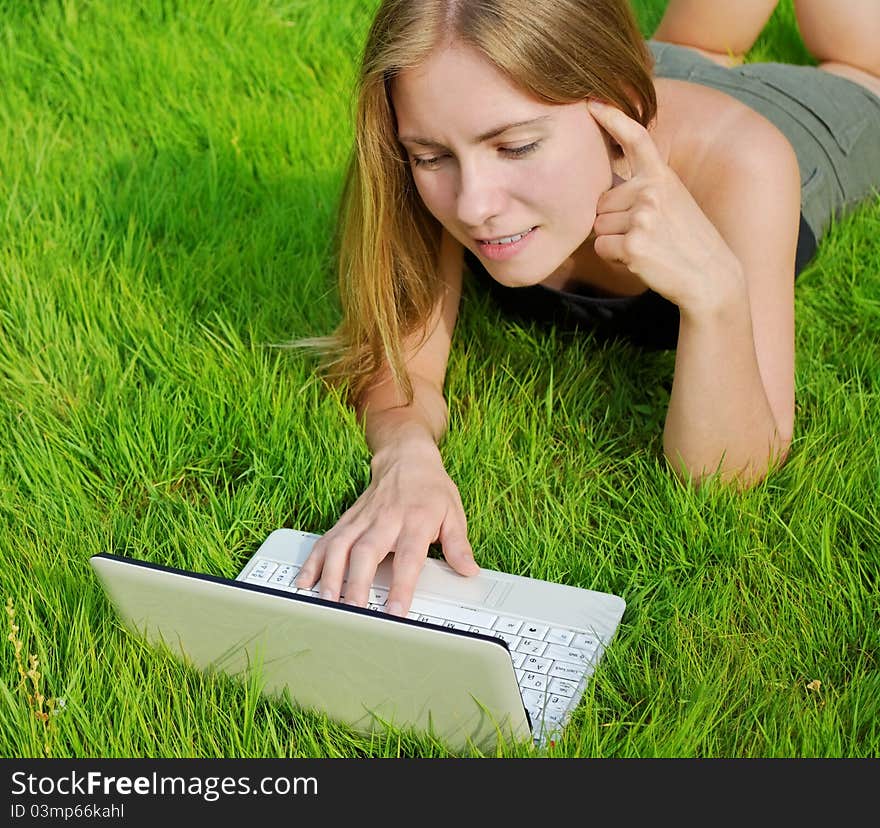 Girl with laptop lying on grass