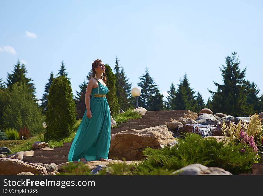 Beautiful brunette walking in the park next to a small waterfall