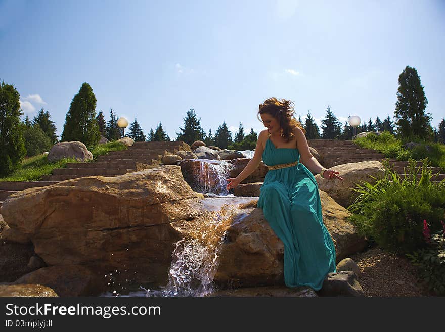 Beautiful brunette walking in the park next to a small waterfall