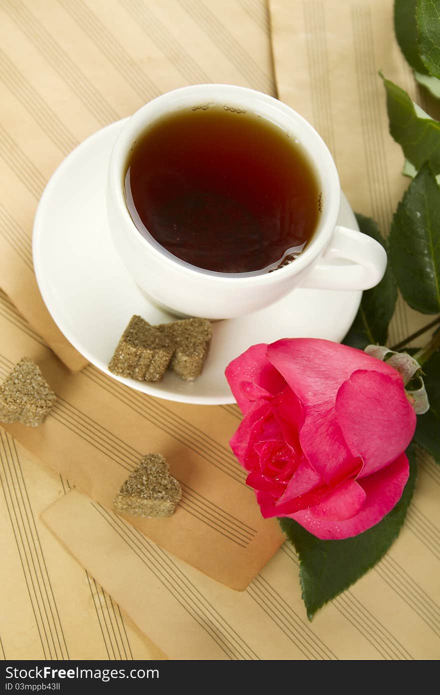 White cup of tea next to sugar and is a beautiful red rose lying on sheets of old paper sheet music. White cup of tea next to sugar and is a beautiful red rose lying on sheets of old paper sheet music