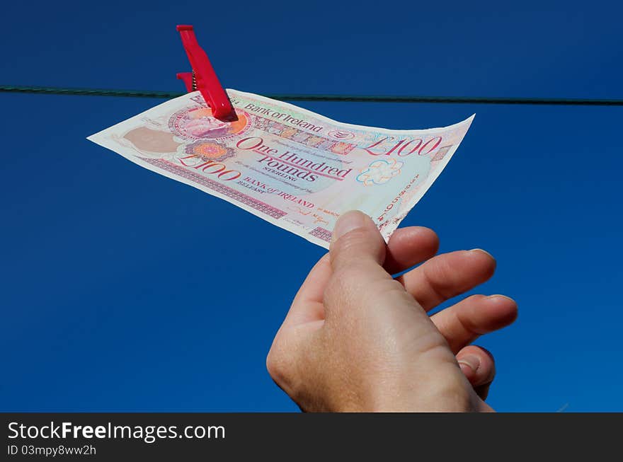 One hundred pound note being plucked from washing line against bright blue sky. One hundred pound note being plucked from washing line against bright blue sky.