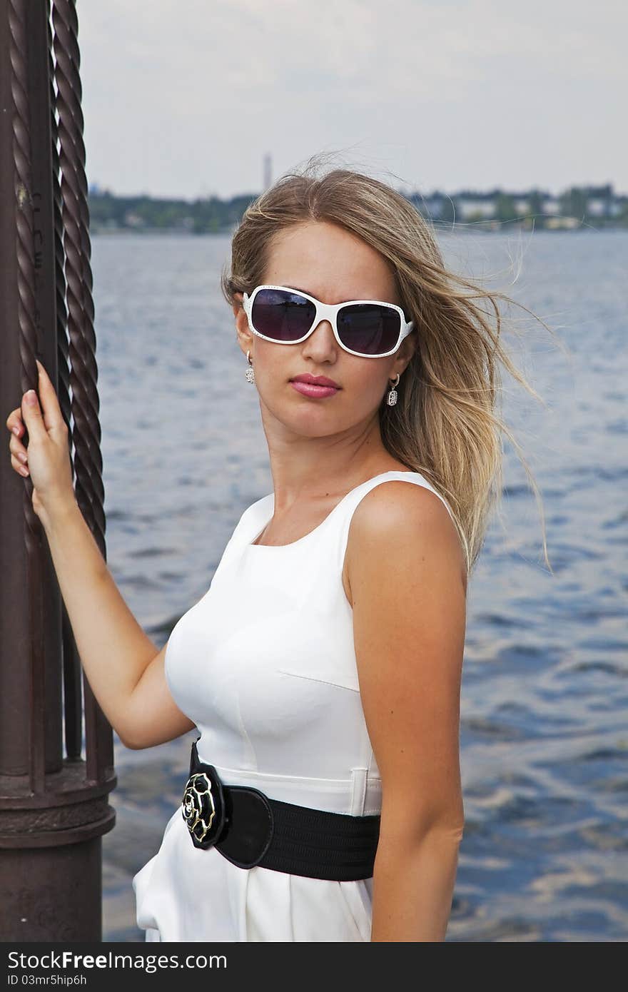 Beautiful blond girl in white dress near the river in summer day